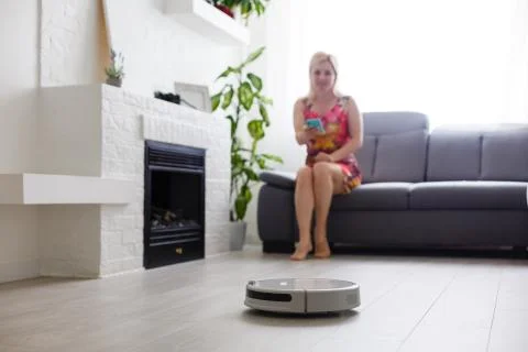 Cleaning concept - automatic robotic hoover clean the room while woman relaxing Foto stock