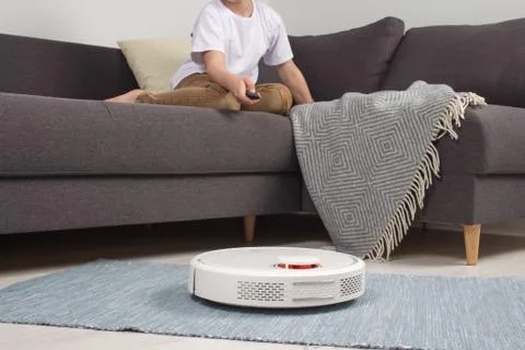 Cleaning concept - boy turn on automatic robotic vacuum cleaner in modern liv Stock Photos
