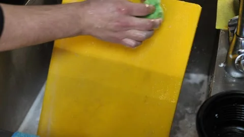 Cleaning a cutting board in a sink with soap and water during kitchen work. men Stock Footage 297127400