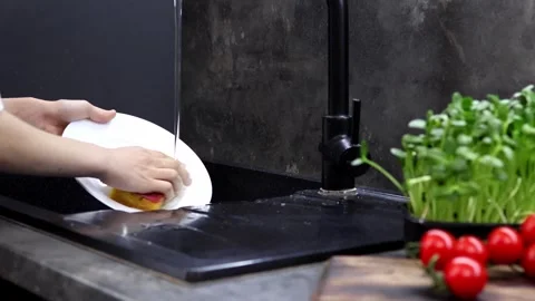 Cleaning dishes while enjoying fresh produce in a modern kitchen Vídeos de archivo 296314617
