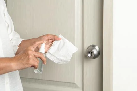 Cleaning door knob with alcohol spray for Covid-19 Coronavirus prevention Stock Photos