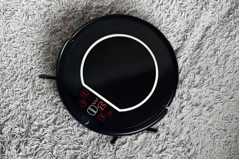 Cleaning fleecy carpet with an automatic vacuum cleaner. Robot vacuum cleaner on Stock Photos
