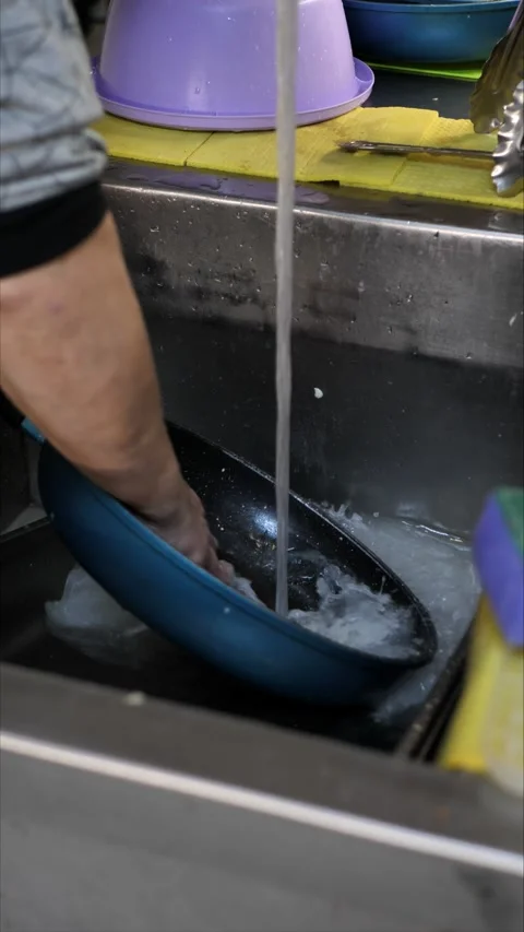 Cleaning a frying pan with bare hands in a sink with soap and water while Stock Footage 305988683