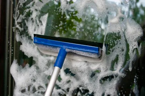 Cleaning glass of window using a squilgee with soap foam. Housekeeping concep Stock Photos
