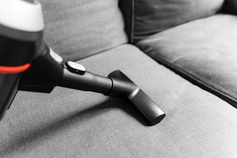 Cleaning grey sofa with wireless vacuum cleaner. Handheld cordless cleaner Stock Photos