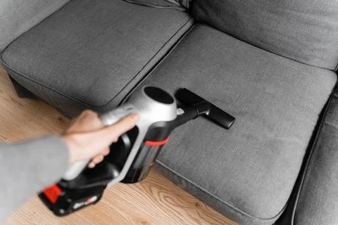 Cleaning grey sofa with wireless vacuum cleaner. Handheld cordless cleaner Stock Photos