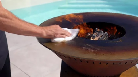 Cleaning hot grill surface as flames rise from center fire Stock Footage 323873028