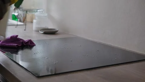 Cleaning Induction Cooktop with Spray Detergent and Microfiber Cloth in Kitchen Stock Footage 345834612