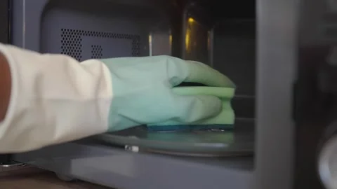Cleaning a microwave with gloves and a sponge in a kitchen Stock Footage 346269868