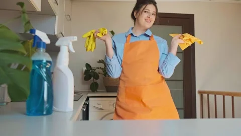 Cleaning professional in uniform stands in kitchen holding cleaning products, re Stock Footage 301868267