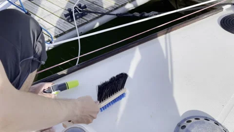 Cleaning sailboat deck with brush and water hose on sunny day Stock Footage 278283053