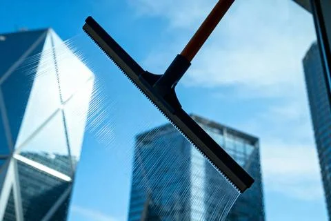 Cleaning a skyscraper window with a squeegee against a blue sky Stock Photos