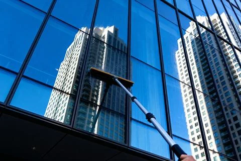 Cleaning skyscraper windows with a long-handled squeegee on a sunny day Stock Photos
