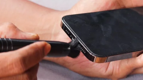 Cleaning a smartphone speaker grille with a small cleaning brush Stock Footage 343512655