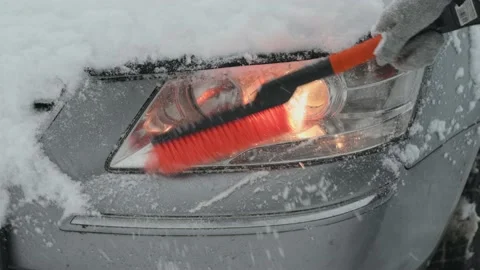 Cleaning snow from the headlight of a car with a brush during a snowfall. Snow Stock Footage 234201193