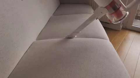 Cleaning a sofa with a handheld vacuum in a cozy living room setting Stock Footage 299153014