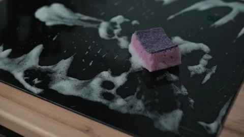 A cleaning sponge sits on a black surface covered with foam and water droplets. 스톡 동영상 337112169