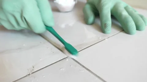 Cleaning tile grout with a toothbrush and gloves in a home setting Stock Footage 346113936