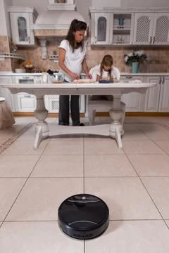 Cleaning with a vacuum while cooking in the kitchen with family brings joy and Stock Photos