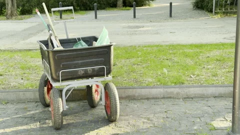 Cleaning wagon sits idle on a cobblestone path by a bright park lawn Stock Footage 336936706