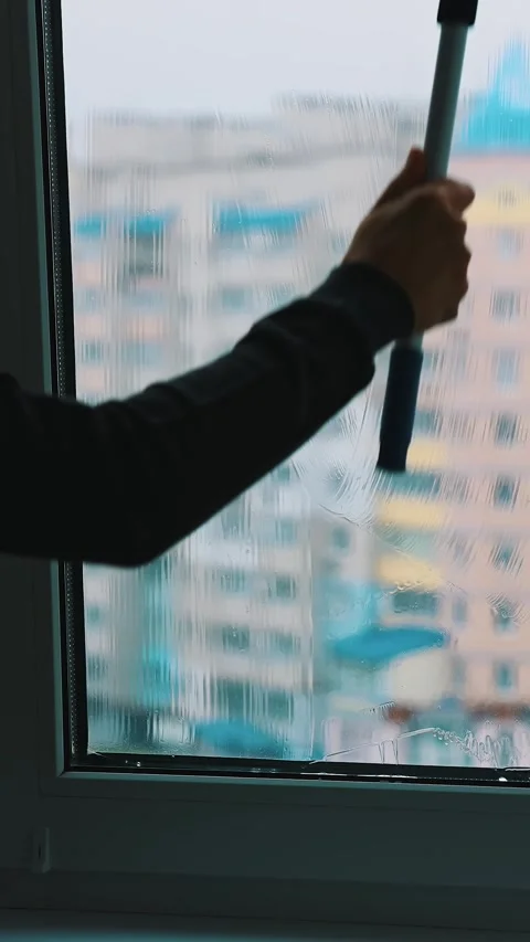 Cleaning window with squeegee on rainy day, apartment buildings in background Video stock 337634477