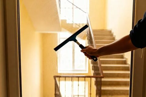 Cleaning a window with a squeegee, view of a staircase in the background Stock Photos