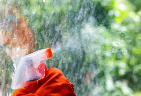 A cleaning worker washes a dirty window with detergent from a spray bottle. Stock Photos