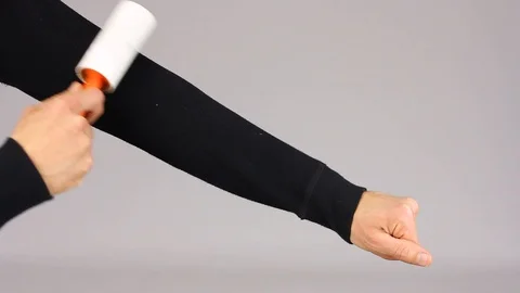 Cleans clothes sleeve with adhesive roller to cleaning cloth, gray background Stockbeeldmateriaal 102889943