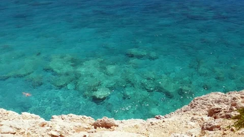 Clear blue ocean with rocks at the bottom. Some people swim in the water. Stock Footage 240341463