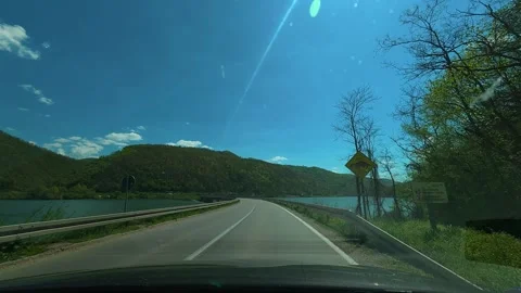 Clear blue sky above winding road beside lake. Balkan, Eastern Europe, POV Vidéo 333344790