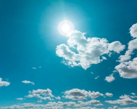Clear blue sky with clouds and sun flare Stock Photos