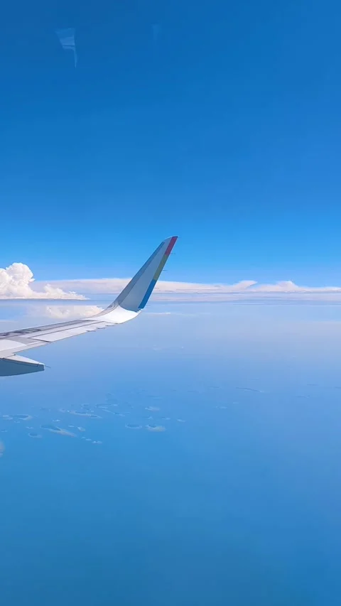 Clear blue sky filled with fluffy clouds, with visible aircraft wing 스톡 동영상 312730420