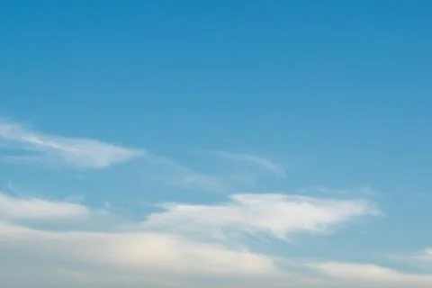 Clear blue sky with soft wispy white clouds drifting diagonally across the Stock Photos