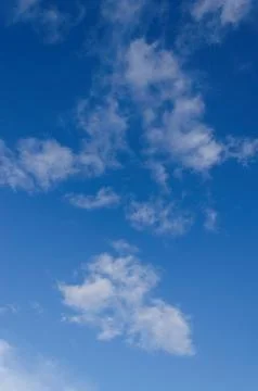 A clear blue sky with sparse white fluffy clouds Stock Photos
