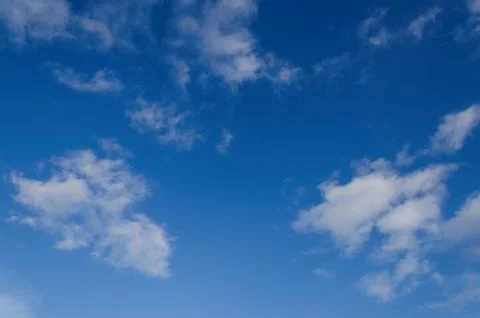 A clear blue sky with sparse white fluffy clouds Stock Photos