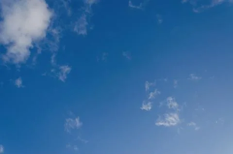 A clear blue sky with sparse white fluffy clouds Stock Photos