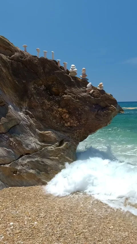 Clear blue waters splash at shaped polished rock with small white stones stacks Stock Footage 261167817