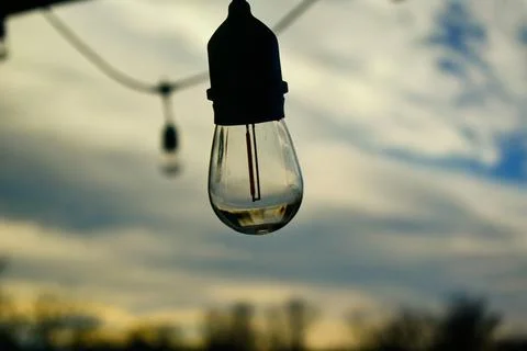 A clear bulb hanging on a string light, unlit, against a clear sky background. Foto stock