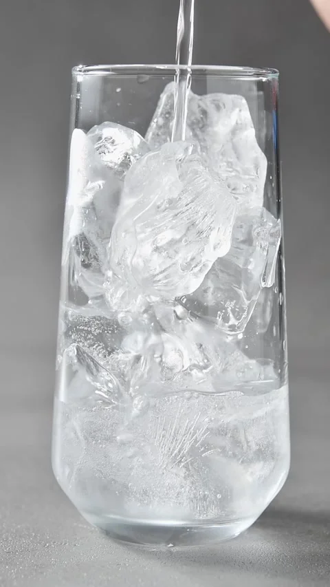 Clear carbonated drink pours over ice in glass on gray background, creating Stock Footage 345486729