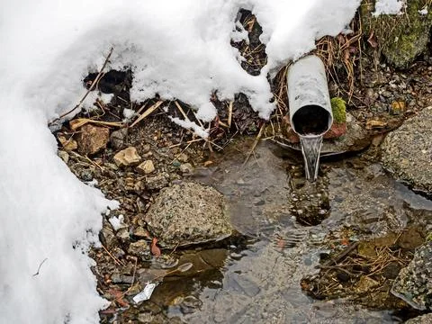 Clear, clean water from a spring source flows from a pipe into a rocky bed Stock Photos