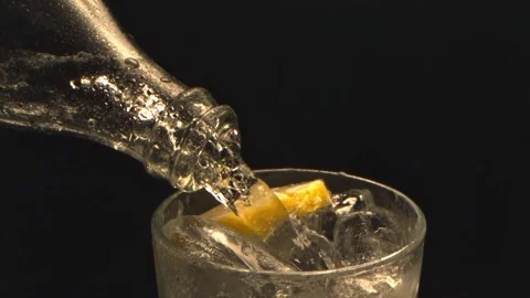 Clear cold drink pouring from transparent bottle into glass with ice cubes and Stock Footage 340953307