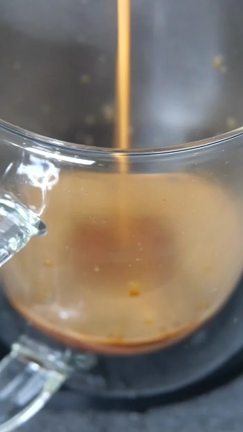 Clear cup of steaming hot coffee being poured into a coffee mug with milk b.. Stock Footage 257900890
