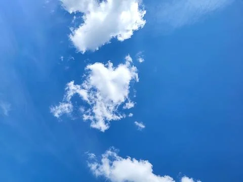 On a clear day, whimsical white clouds drift across the blue sky. Stock Photos