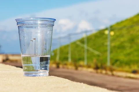 Clear disposable plastic cup with water left on concrete ledge outdoors Stock Photos