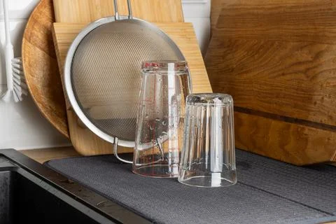 Clear drinking glasses placed upside down on a drying mat near wooden cutti.. Stock Photos