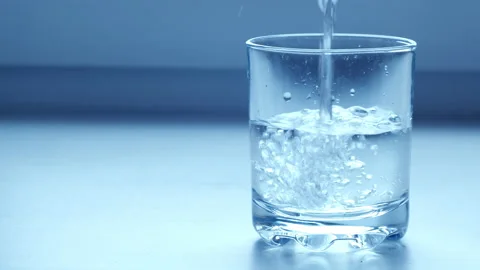 Clear drinking water pouring into glass on blue grey background. Mineral water Stock Footage