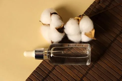 Clear dropper bottle placed next to cotton bolls on a wooden mat in a simple Stock Photos