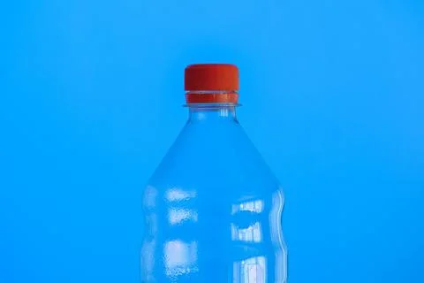 Clear empty plastic bottle with red lid isolated on blue close up detail shot Fotos de archivo