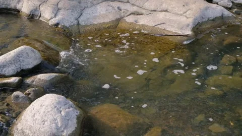 Clear freshwater stream flowing over weathered rock formation into shallow p Stock Footage 342959979