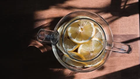 A clear glass container filled with sliced lemons and water sits on a wooden Stock Footage 338297729